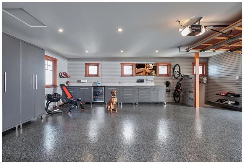 Finished garage with charcoal flake epoxy floor, gray cabinetry and a dog sitting on the coating